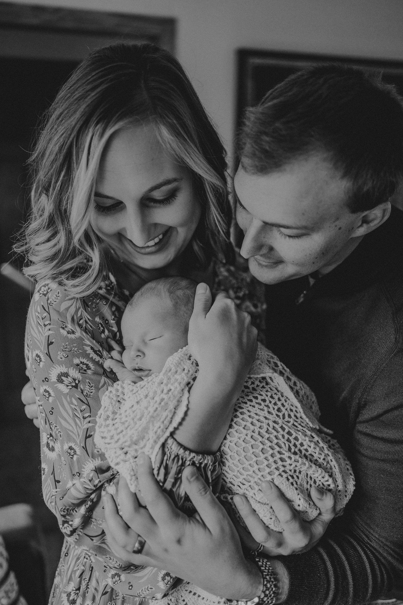 A touching family moment as new parents cradle their sleeping newborn wrapped in a knit blanket.