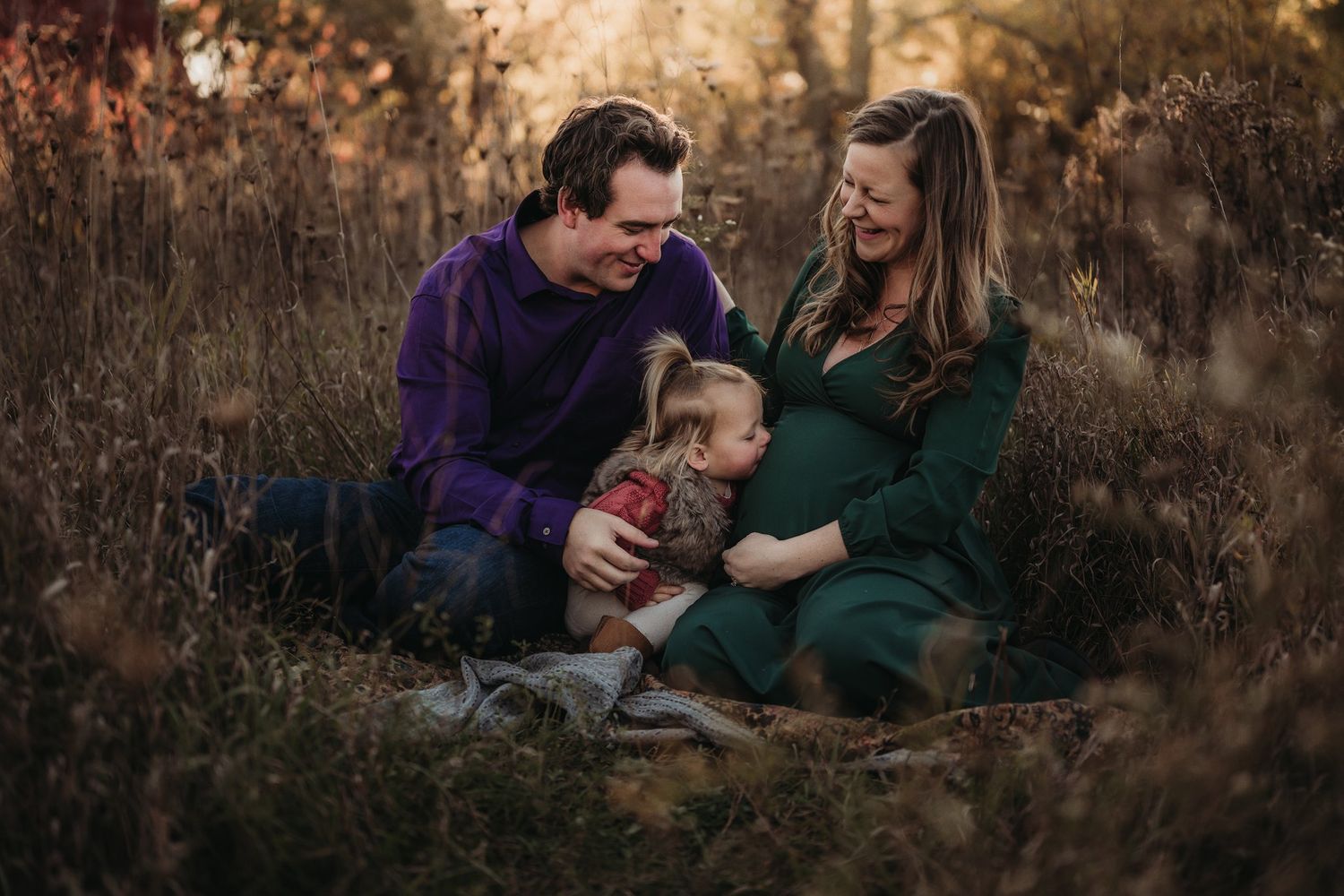 Family sitting together in tall grass during golden hour autumn photoshoot.