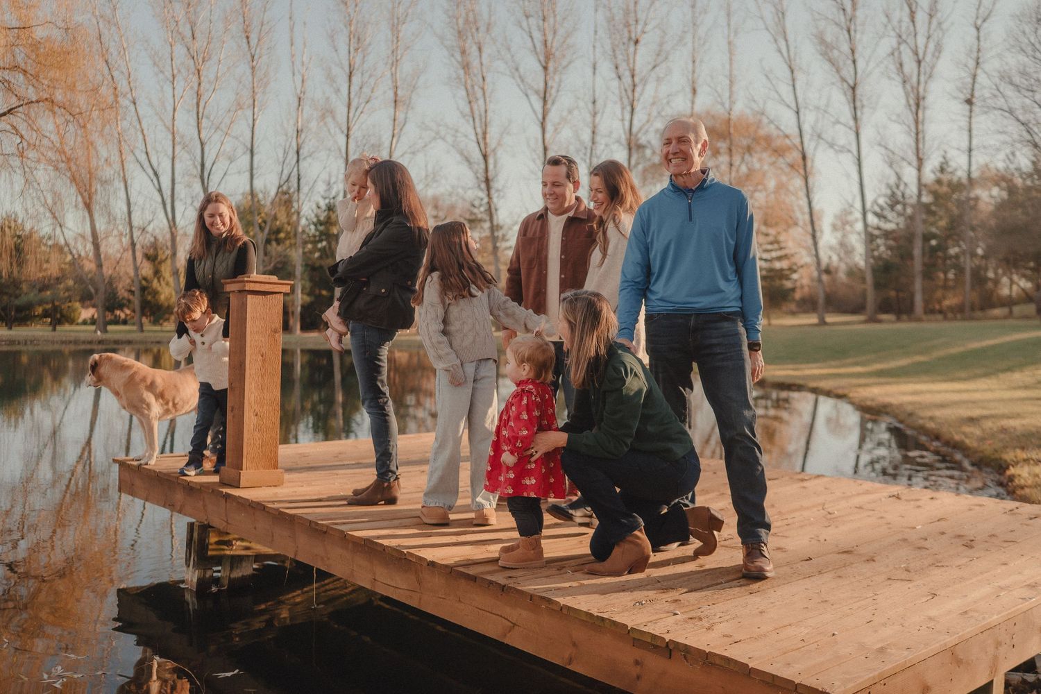 Group gathers on wooden dock by pond during sunset photo session.