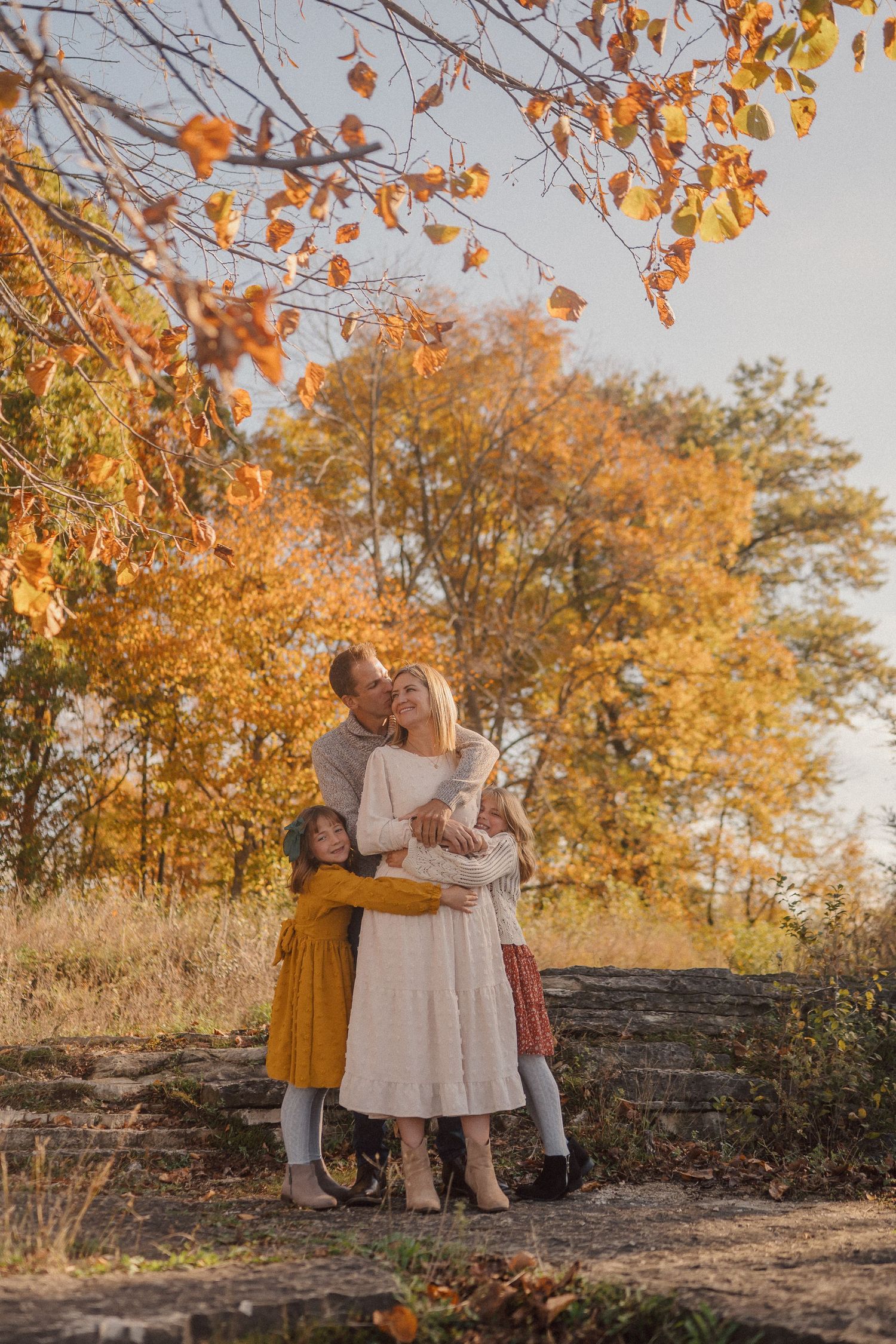 A couple shares an intimate moment against a backdrop of autumn trees with golden leaves at sunset.