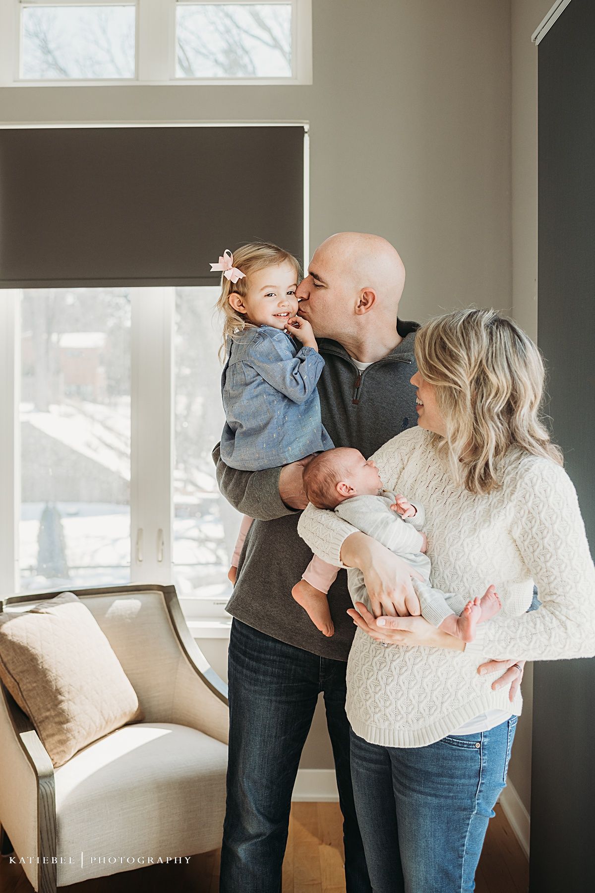 Candid family moment captured in a living room as parents bond with their toddler and newborn.