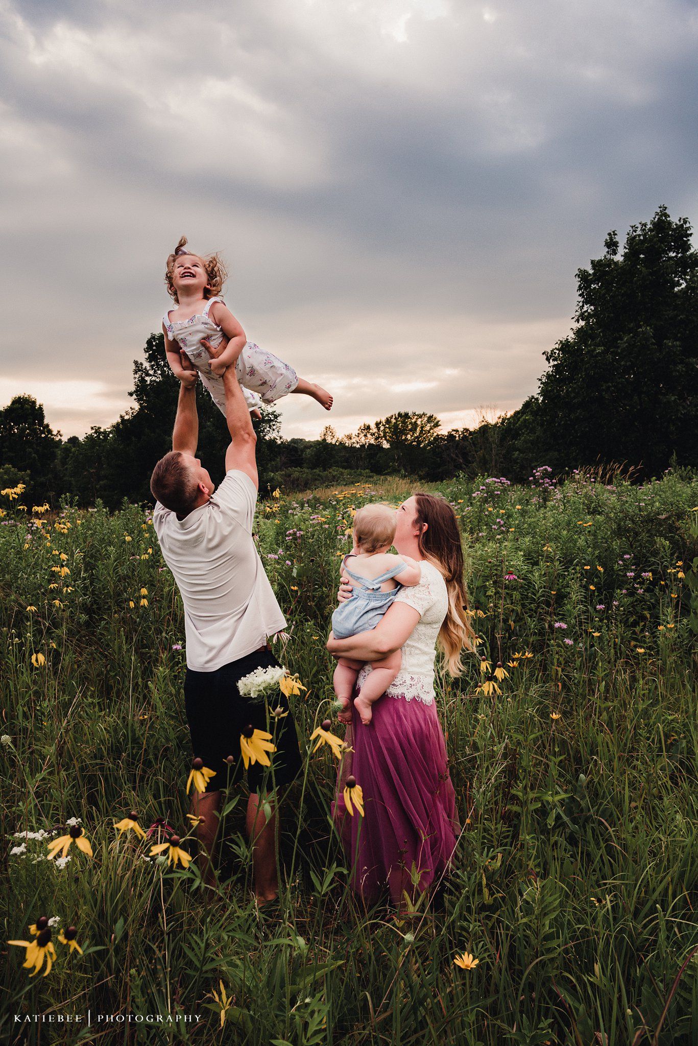 Playful family enjoying time together in a meadow filled with yellow wildflowers at dusk.