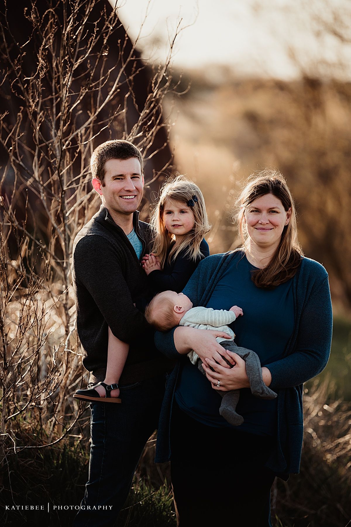 Outdoor family portrait in warm autumn light against natural brush backdrop.