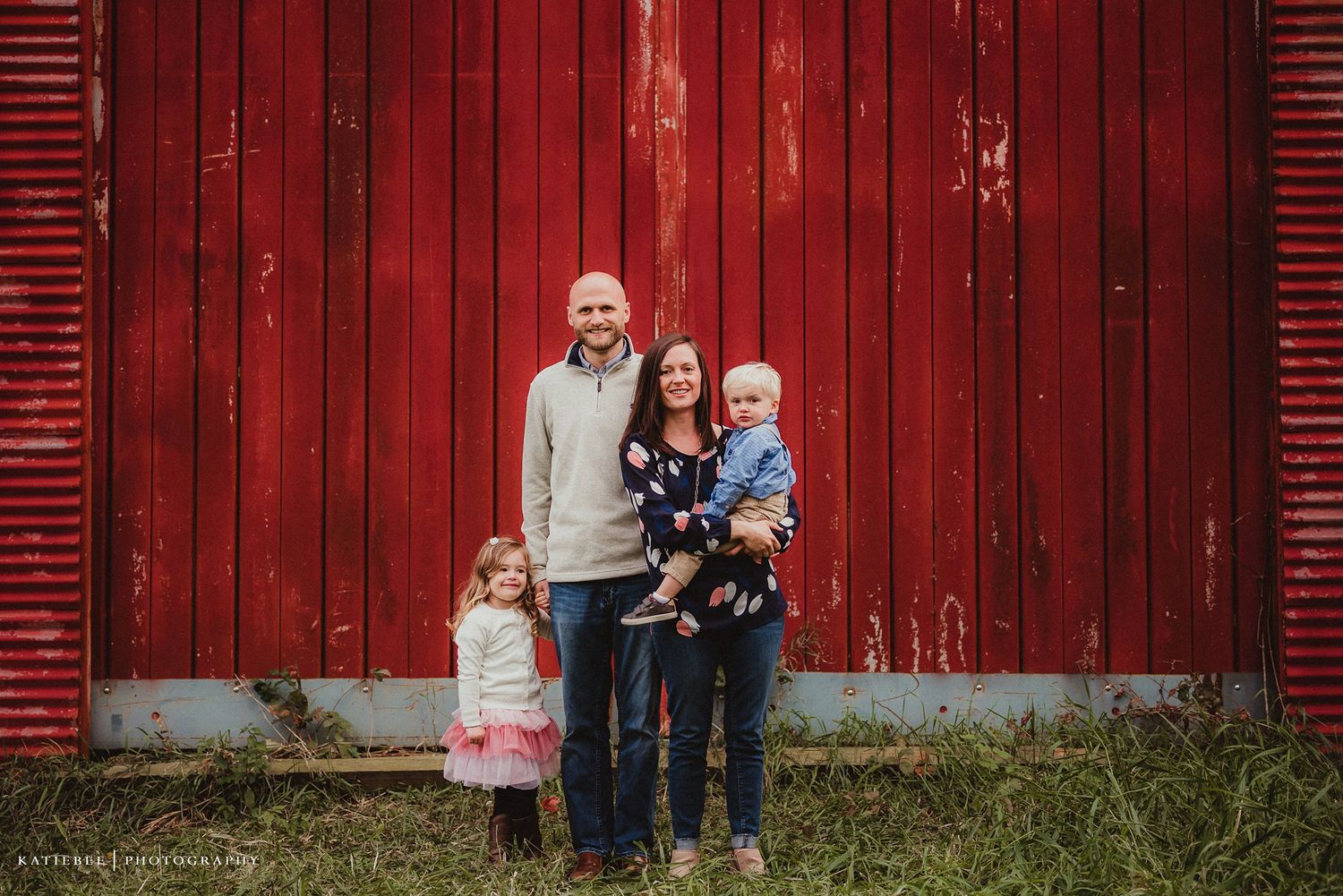 A family portrait captured against the backdrop of a classic red barn.