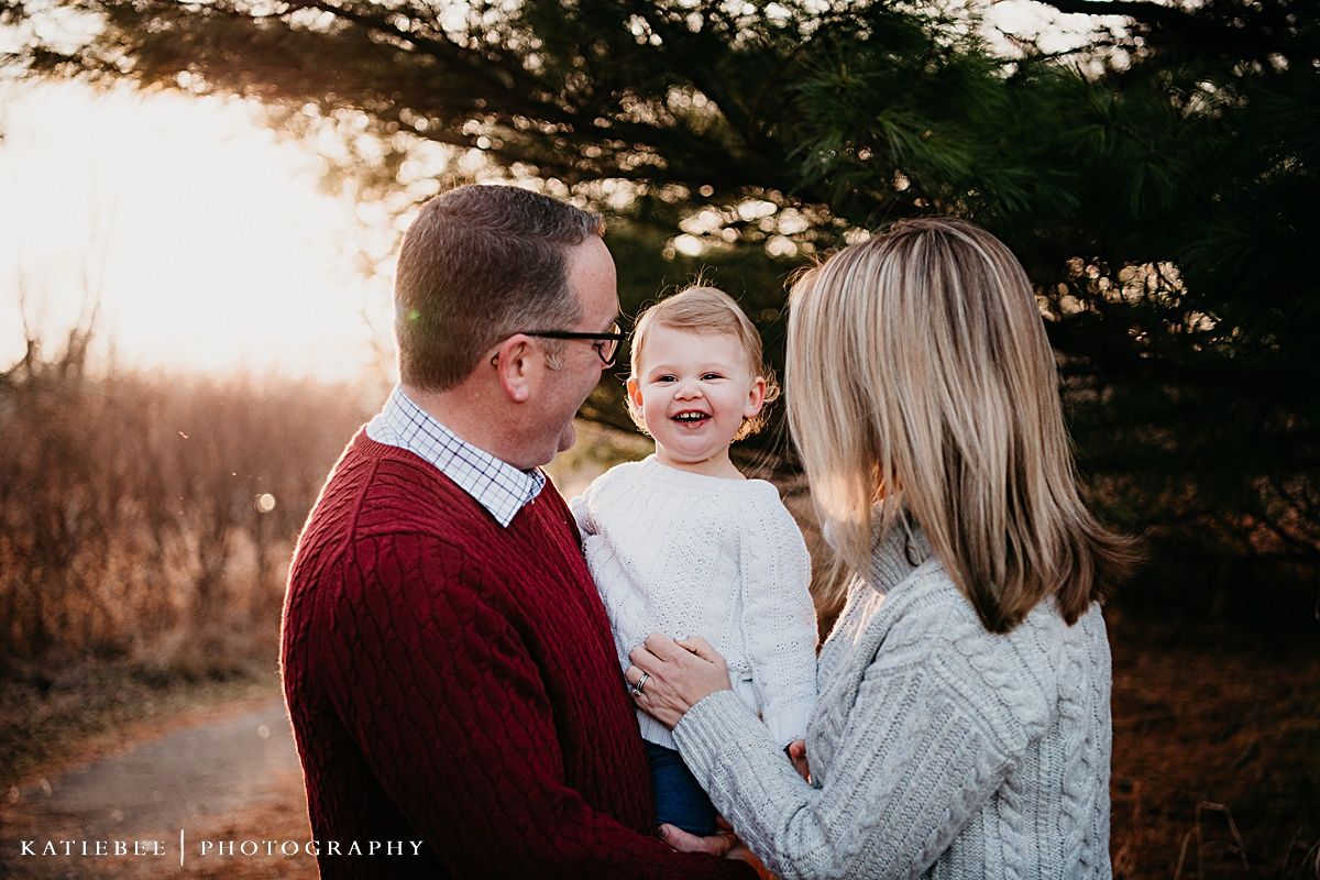 A family shares a joyful moment together outdoors during sunset with pine trees in the background.
