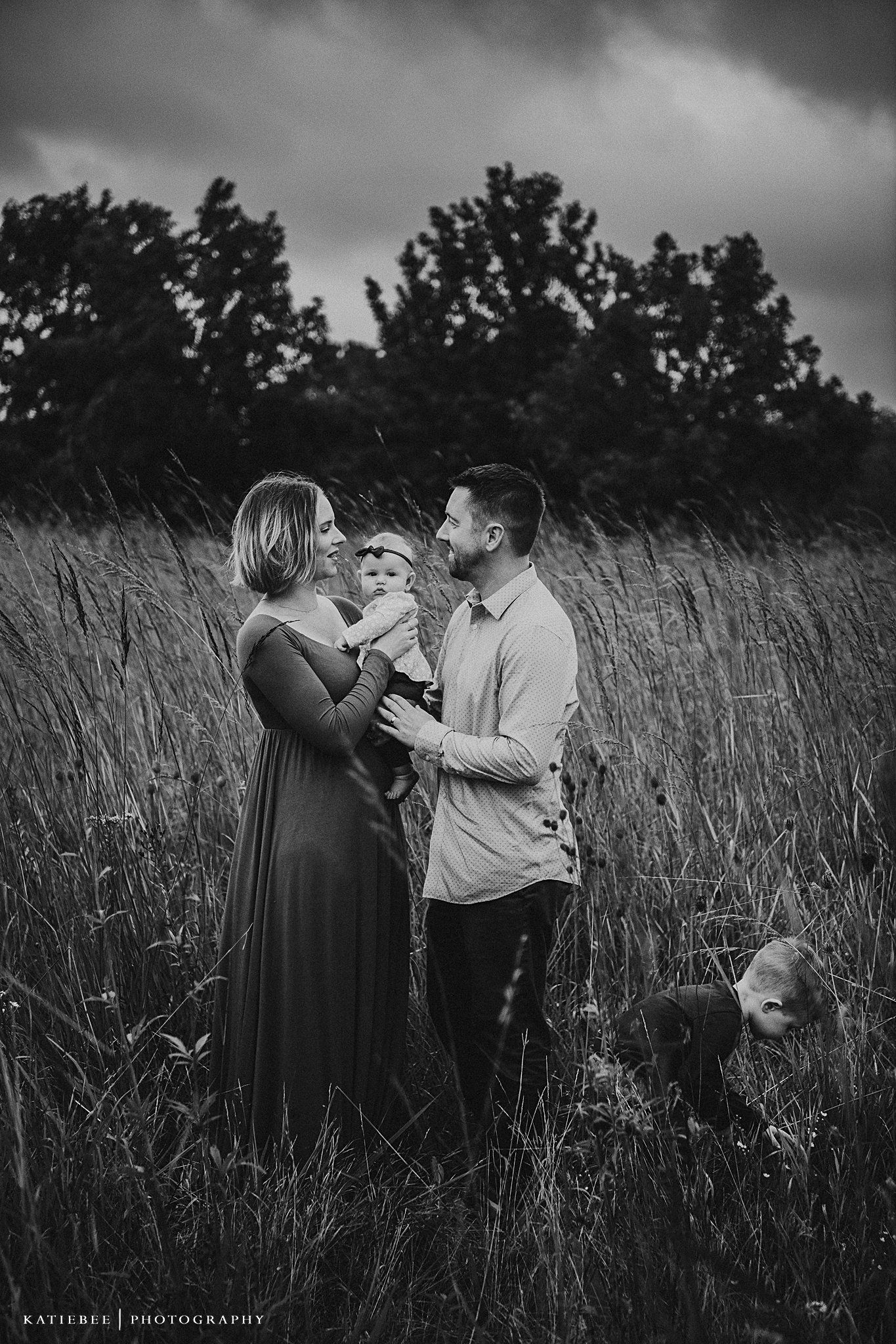 Black and white photo of family sharing tender moment in field of wild grass.