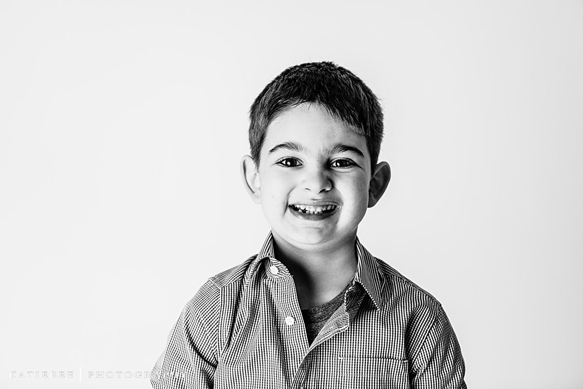 Close-up portrait of child with bright smile in striped shirt against white background.