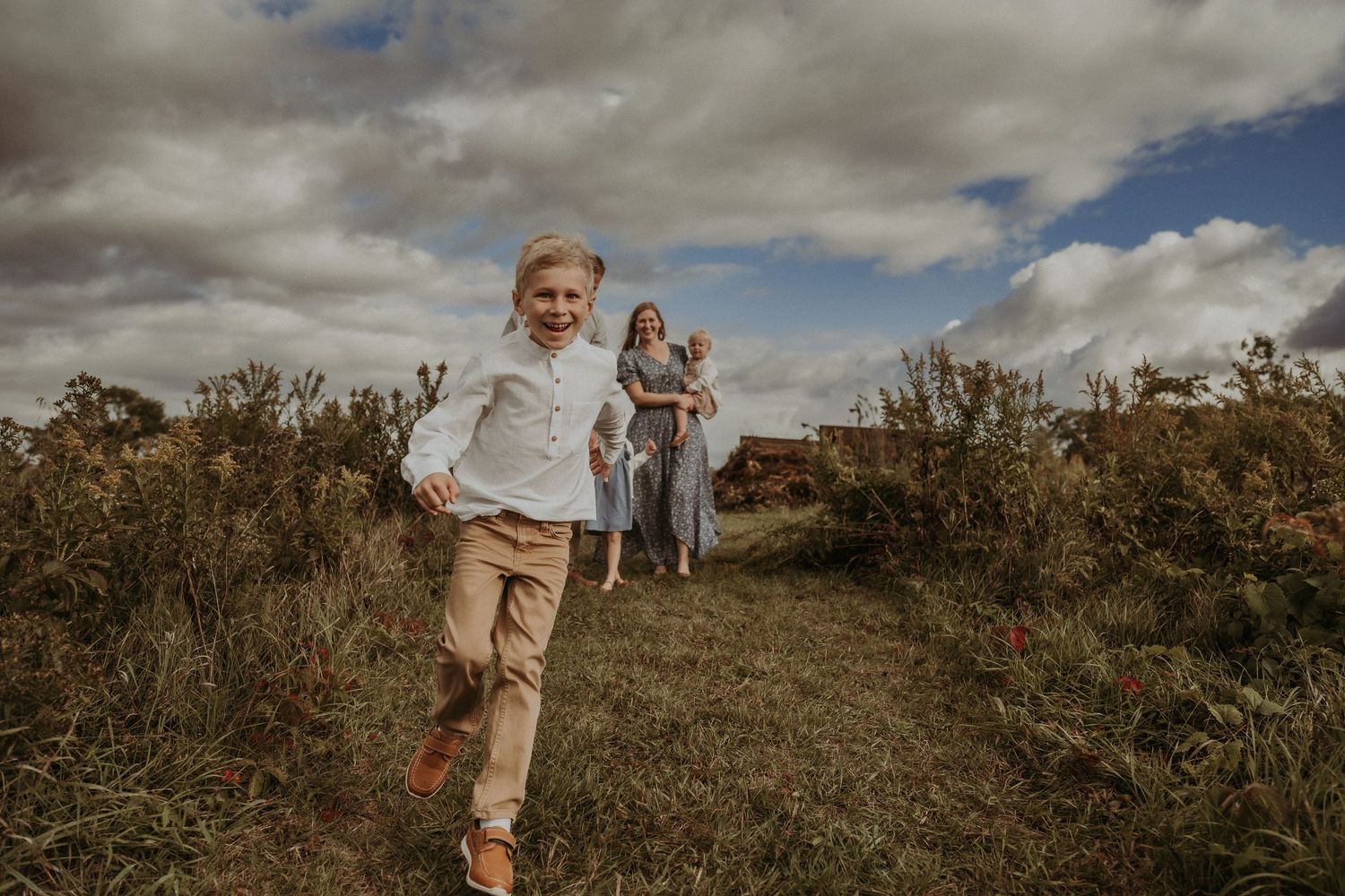 Energetic outdoor family photo session in a natural field setting with dramatic clouds overhead.
