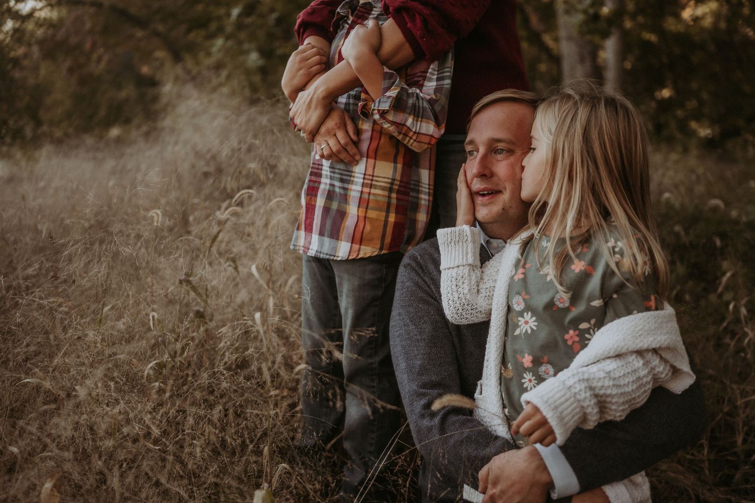 A family wearing cozy sweaters shares an intimate moment together in a golden autumn field at sunset.
