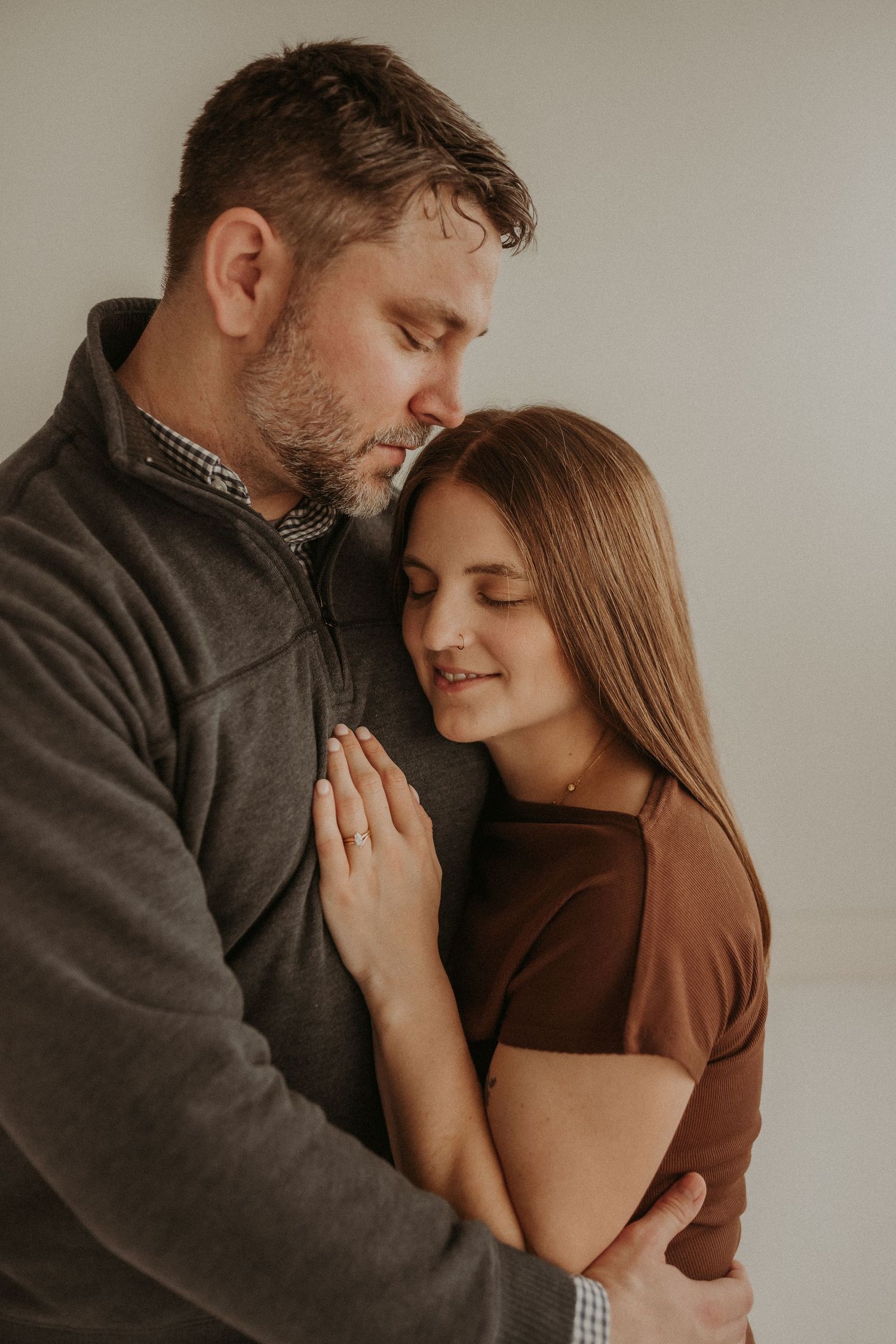 A couple shares an intimate embrace against a white wall background.