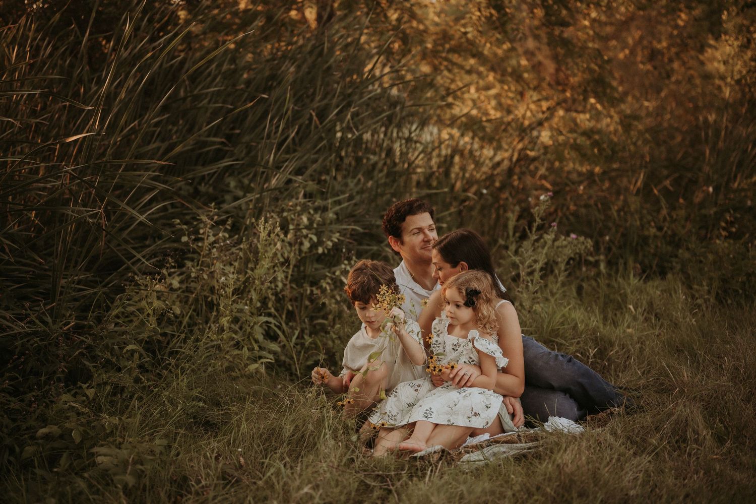 A family shares an intimate moment while sitting in golden grass during sunset.