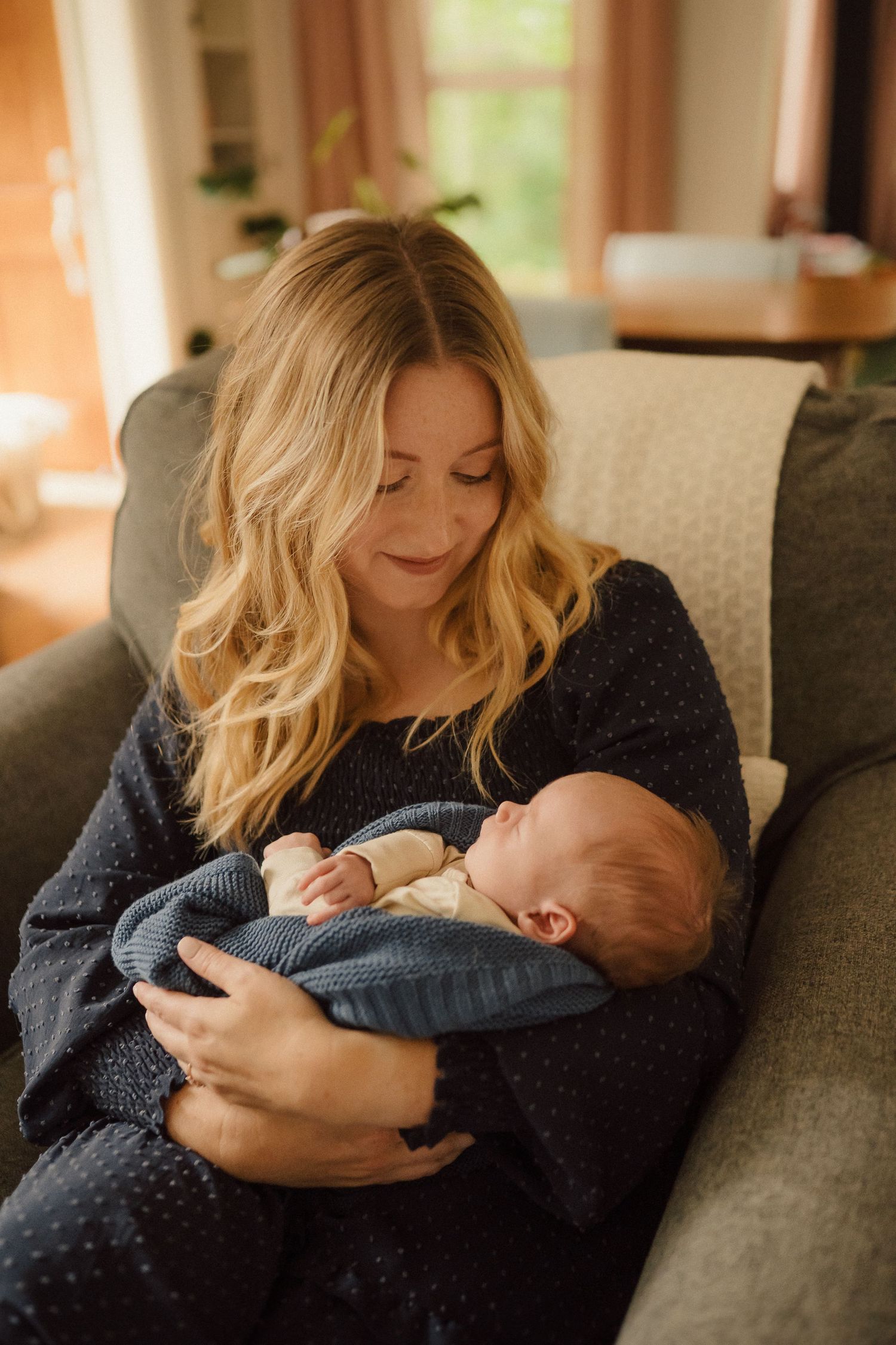 Tender moments shared on grey couch as parents cuddle with newborn baby in cozy home setting.