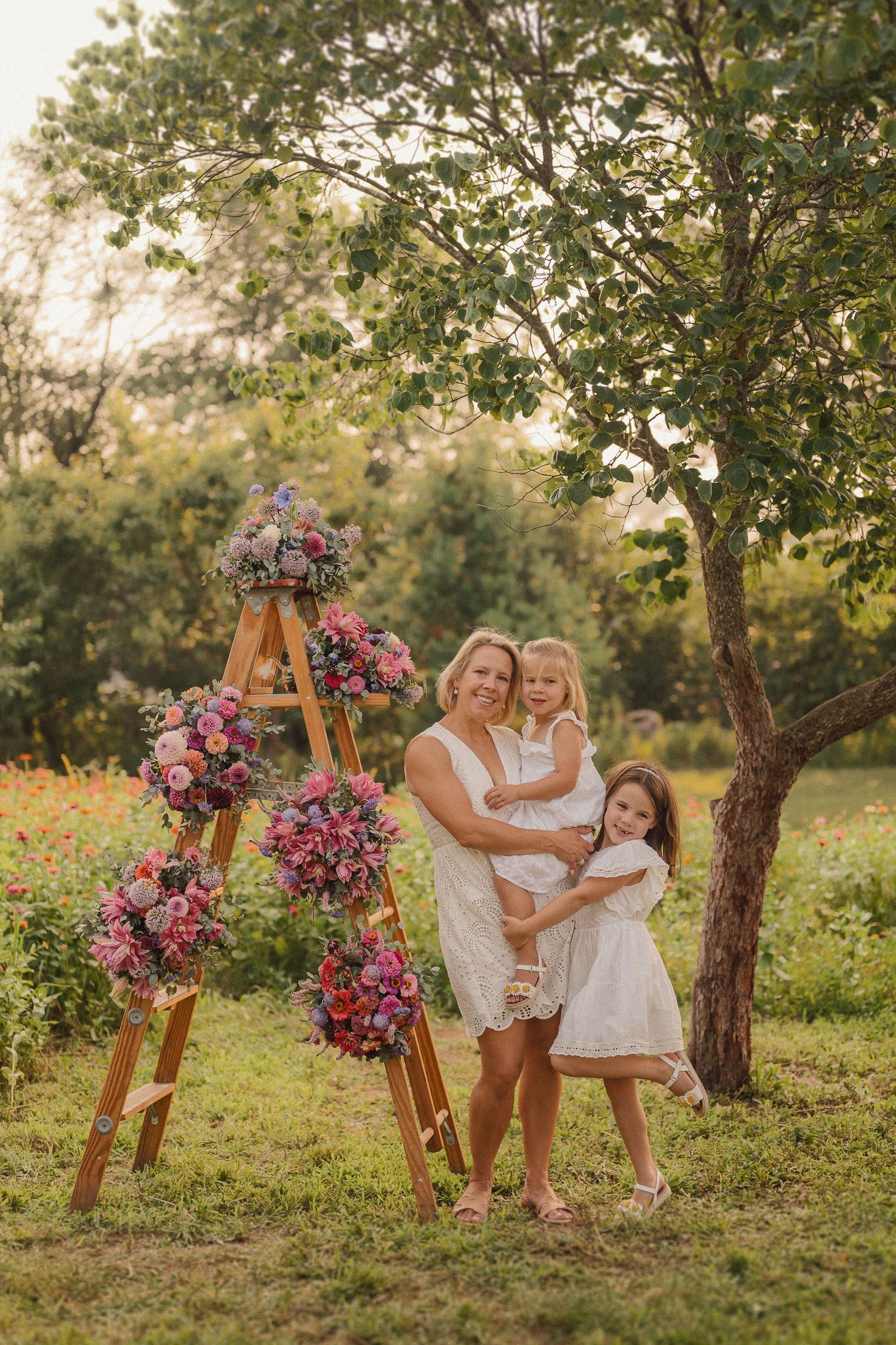 Playful photo session featuring a wooden ladder with vibrant floral decorations in a natural outdoor setting.