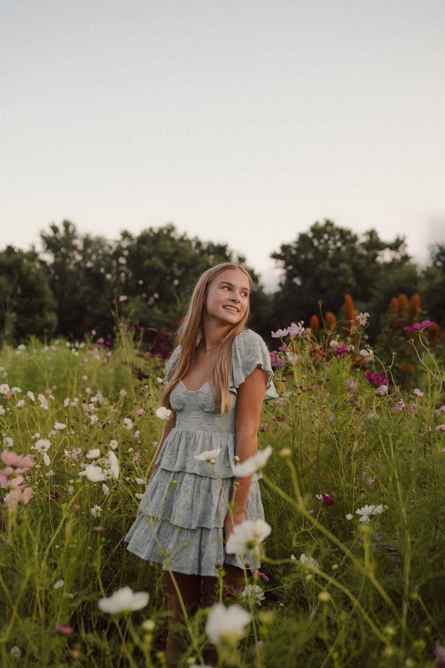 A dreamy scene in a wildflower meadow shows someone in a light blue dress dancing among colorful summer blooms at sunset.
