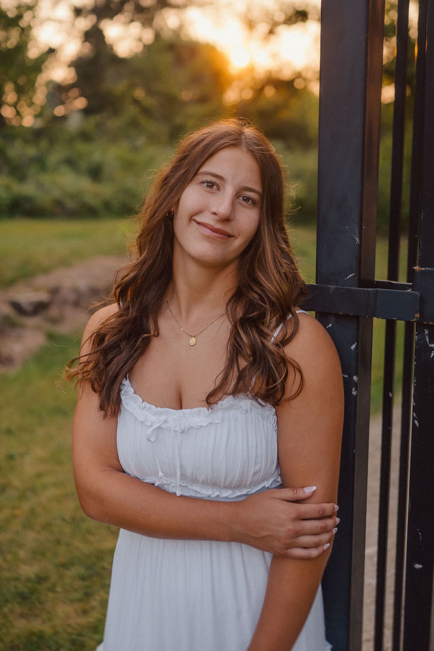 Person in white summer dress poses against black fence during golden hour sunset.