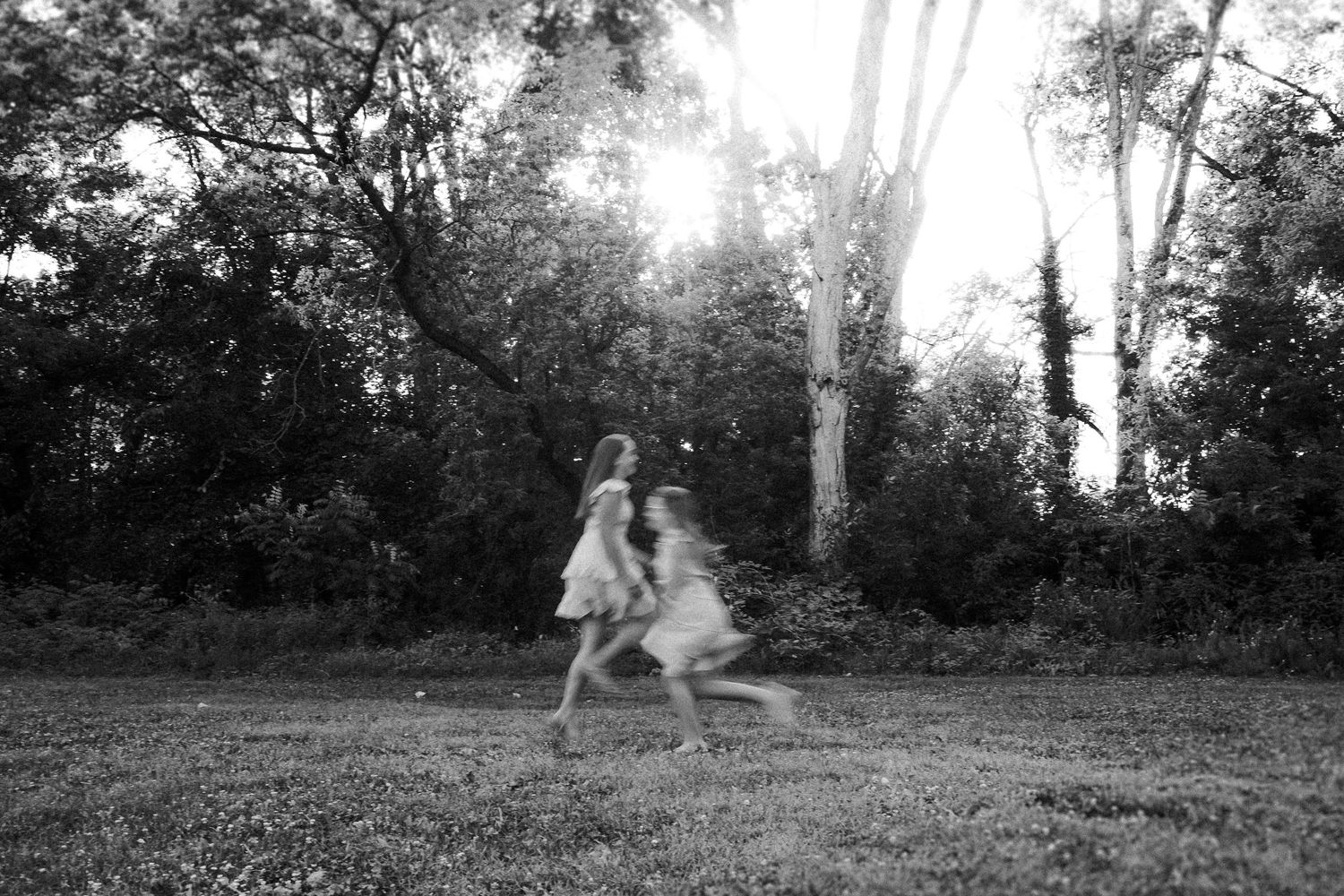 Two people play and dance in an outdoor setting during golden hour, casting long shadows on the grass.
