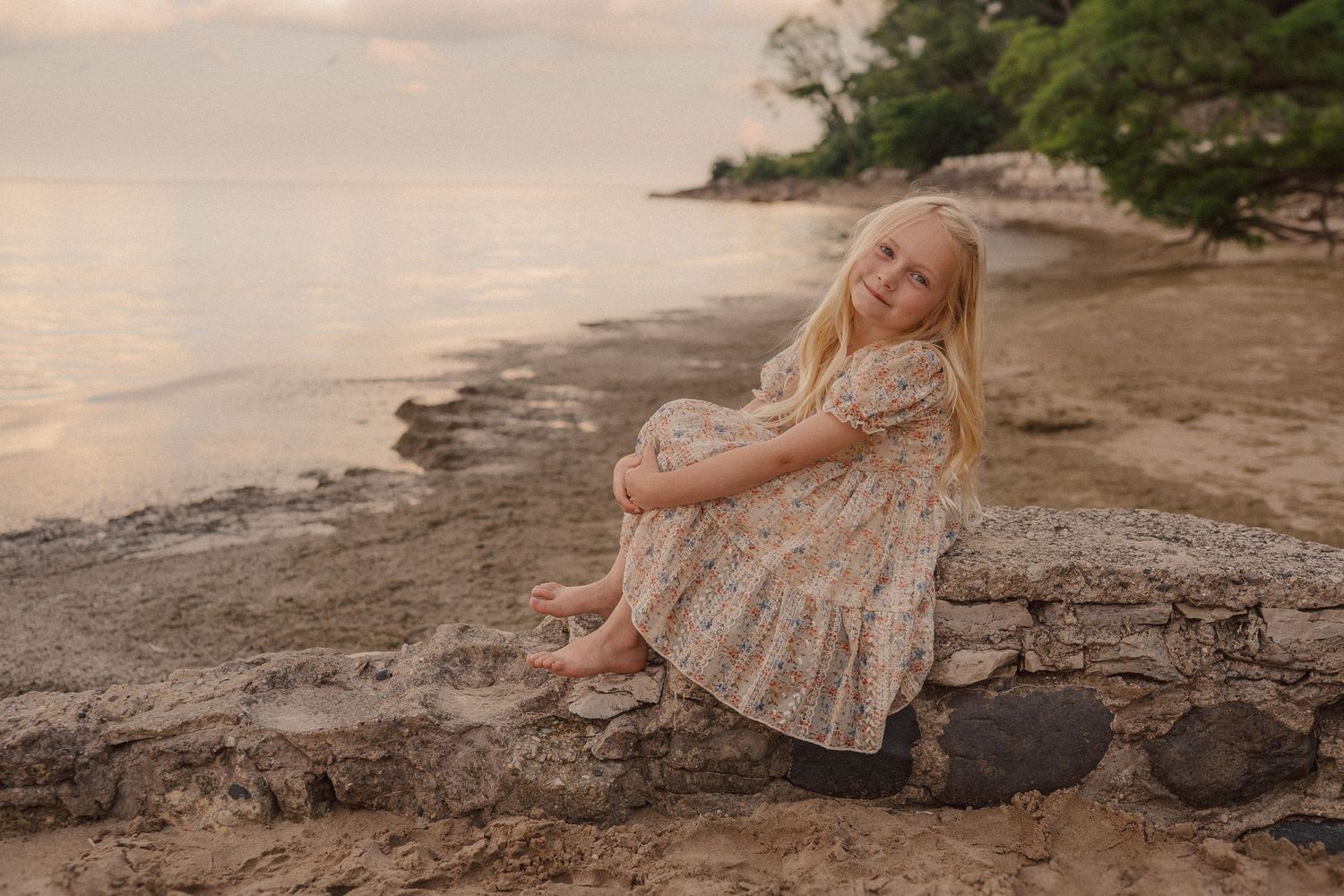 A series of connected images showing someone in a flowy dress posing along rocky coastal cliffs at sunset.