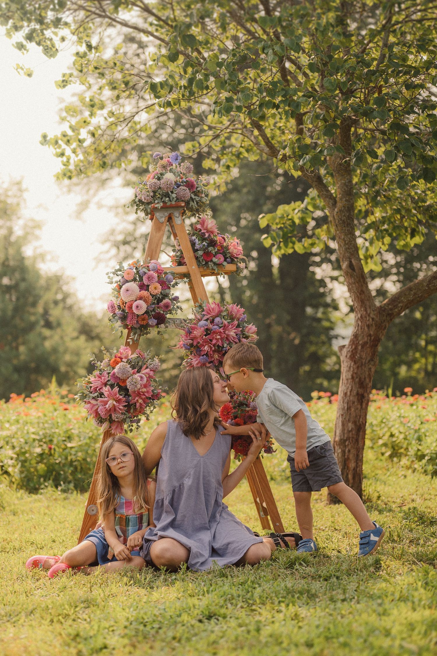 A wooden ladder decorated with pink and red flowers creates a dreamy backdrop for a family photoshoot in a sunny garden.