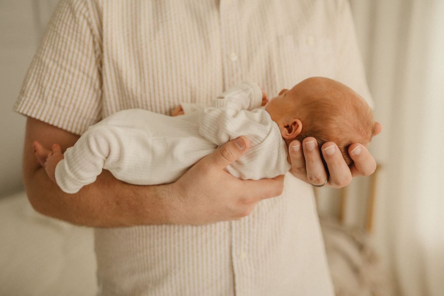 Soft portrait shot of hands delicately supporting a baby dressed in light colored clothing.