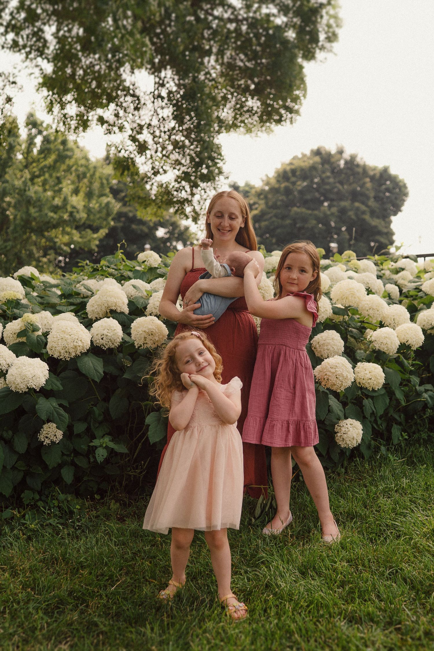 Three people pose playfully against a backdrop of white hydrangea bushes in a summer garden.