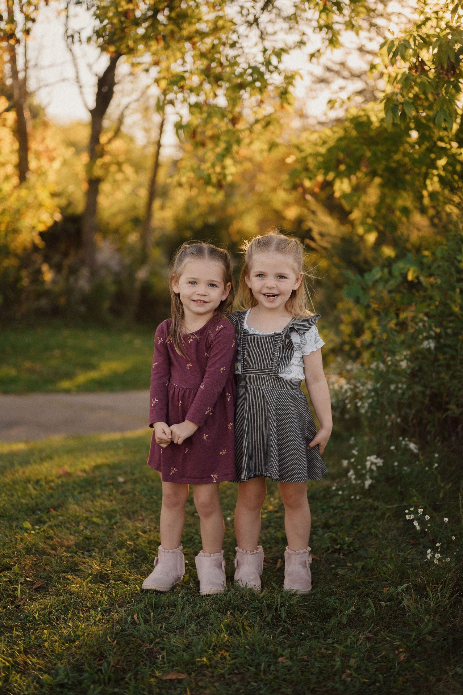 Two young children in dresses sitting together outdoors during golden hour autumn photography.