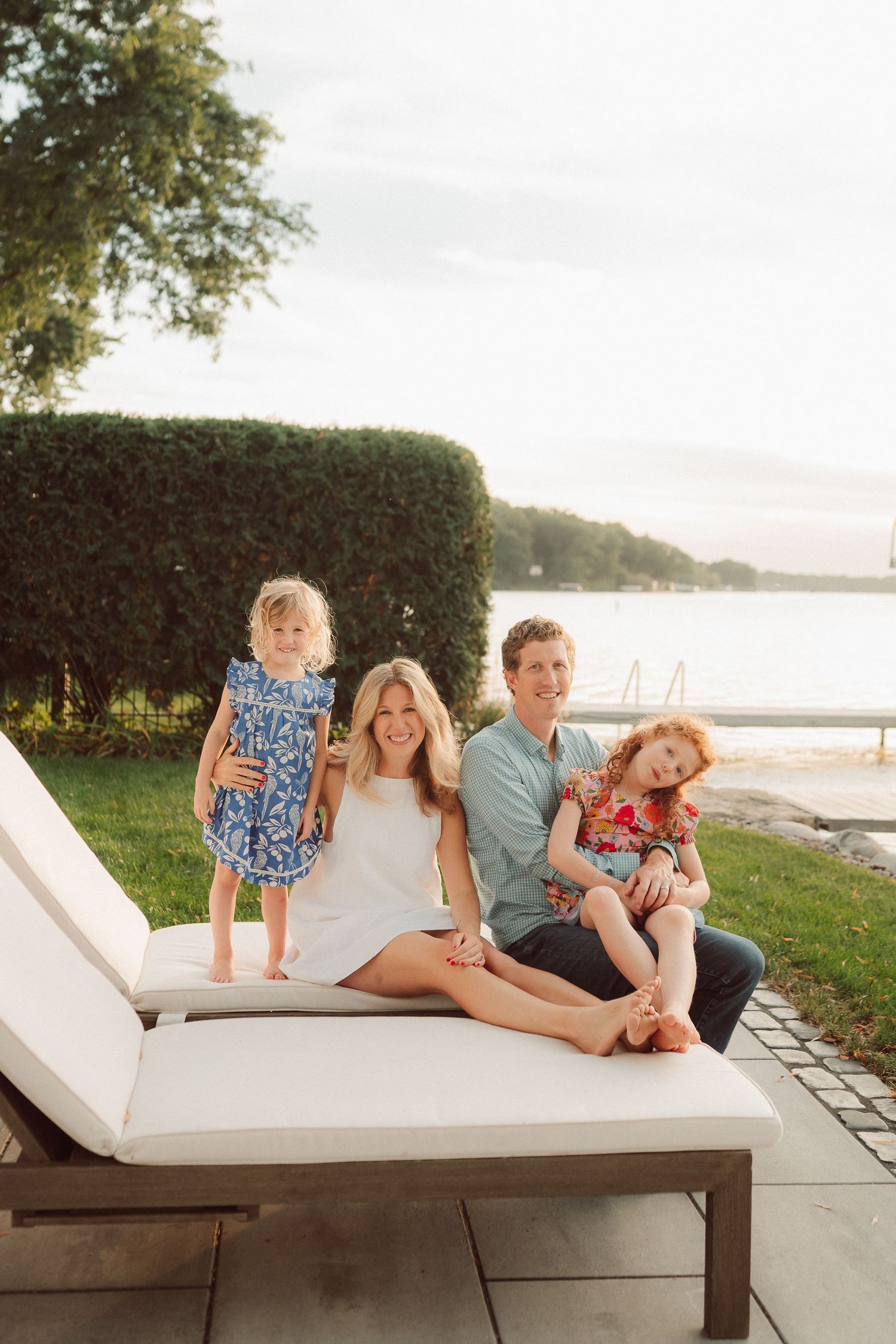 Family relaxing together on a white outdoor lounge chair by the water.