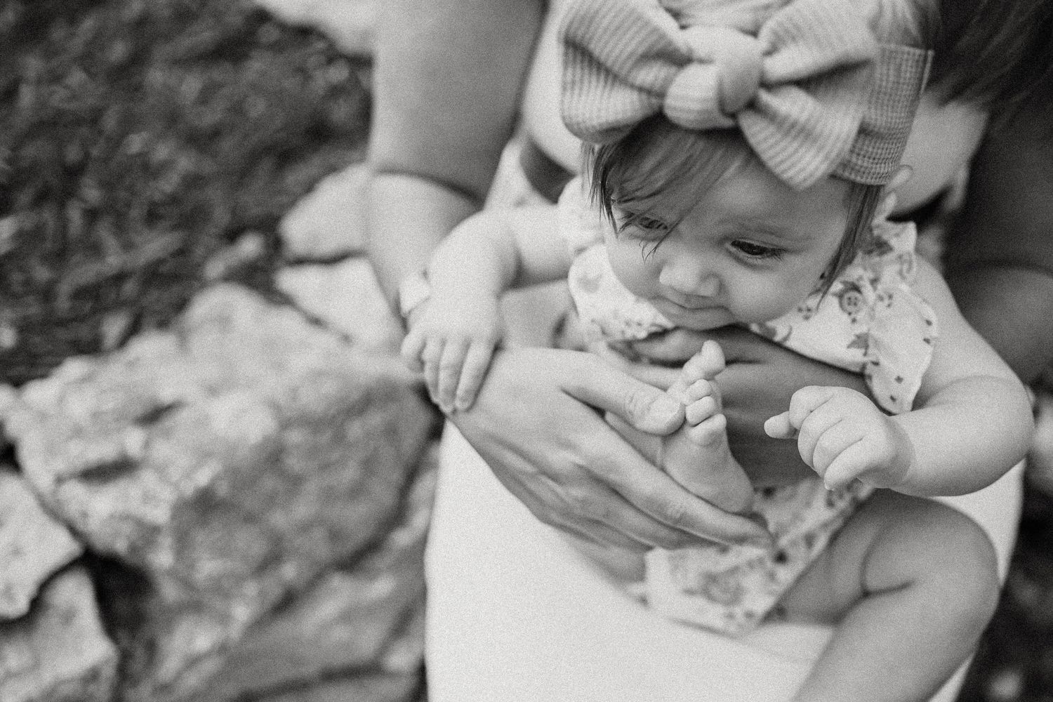 A tender black and white close-up of a small infant wearing a bow headband.