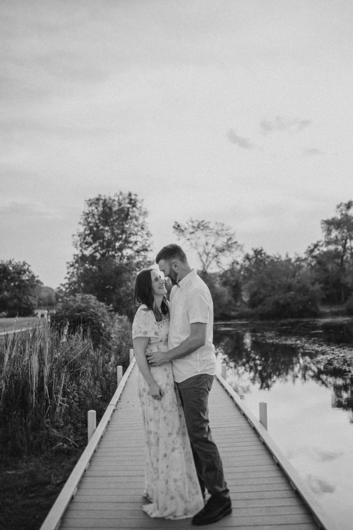 Romantic couple embracing on a wooden dock over a tranquil pond at dusk.