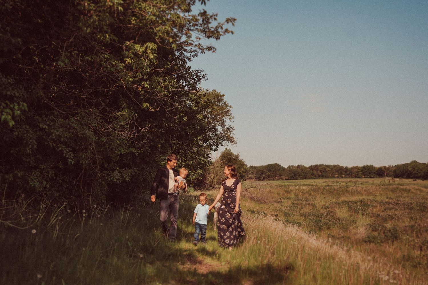 Family walking together along tree line during sunset in rural setting.