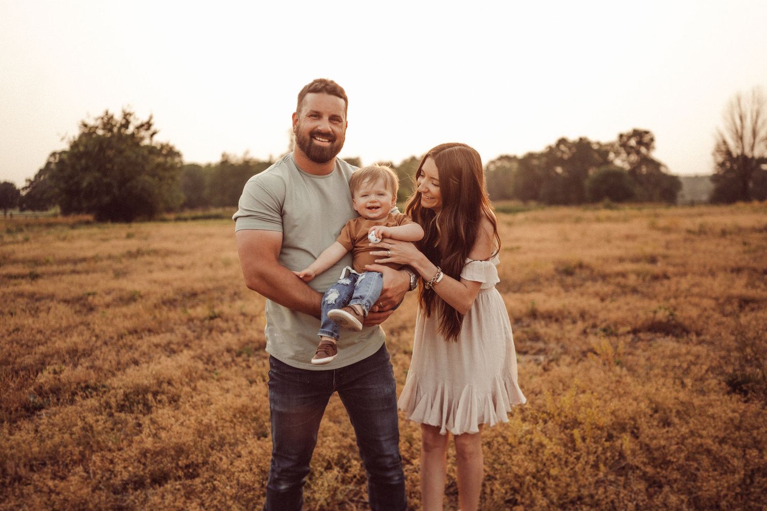 A young family laughs together during their outdoor photo session at golden hour.
