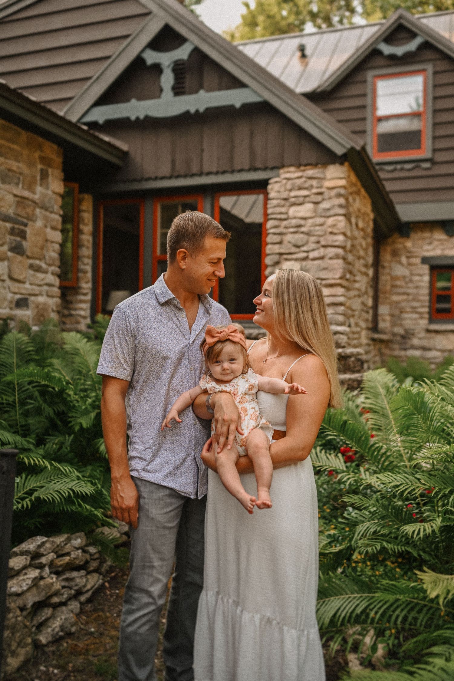 A family portrait in front of a stone cottage with lush ferns in the foreground.