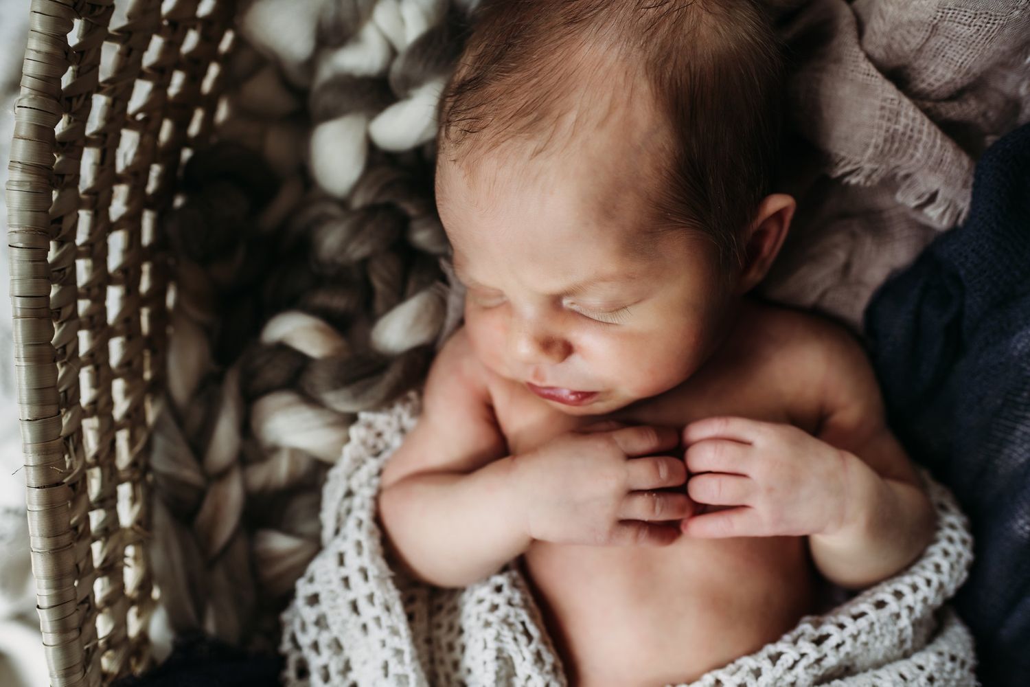 Peaceful sleeping newborn nestled in soft textiles and woven basket.