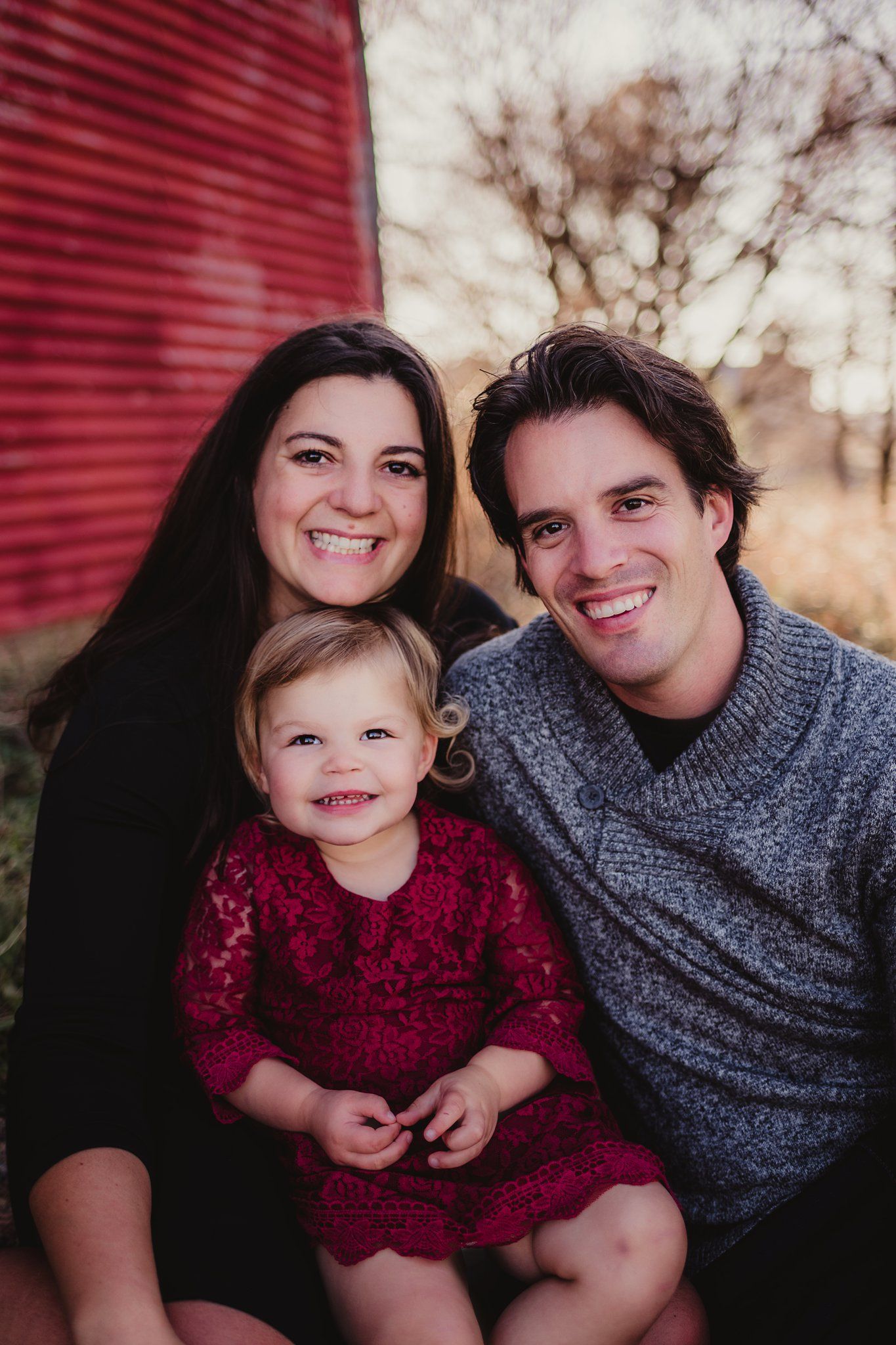 Family portrait with matching outfits against red barn wall during golden hour.
