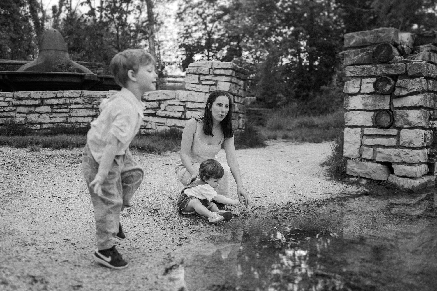 A casual outdoor scene by a stone wall where people gather near a puddle on a summer day.