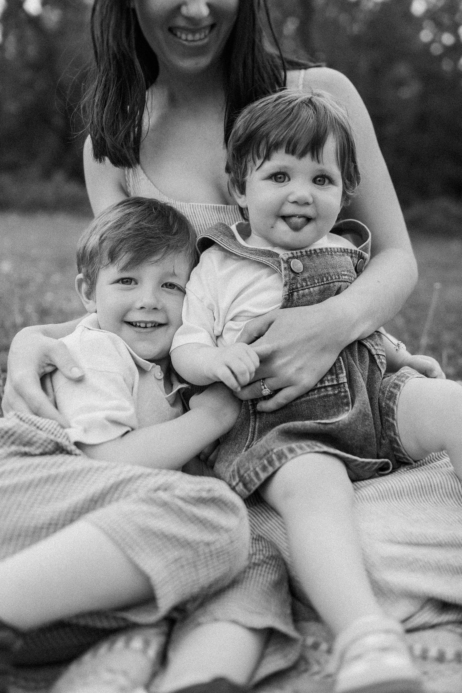 Black and white portrait of joyful young family cuddling together on a picnic blanket outdoors.