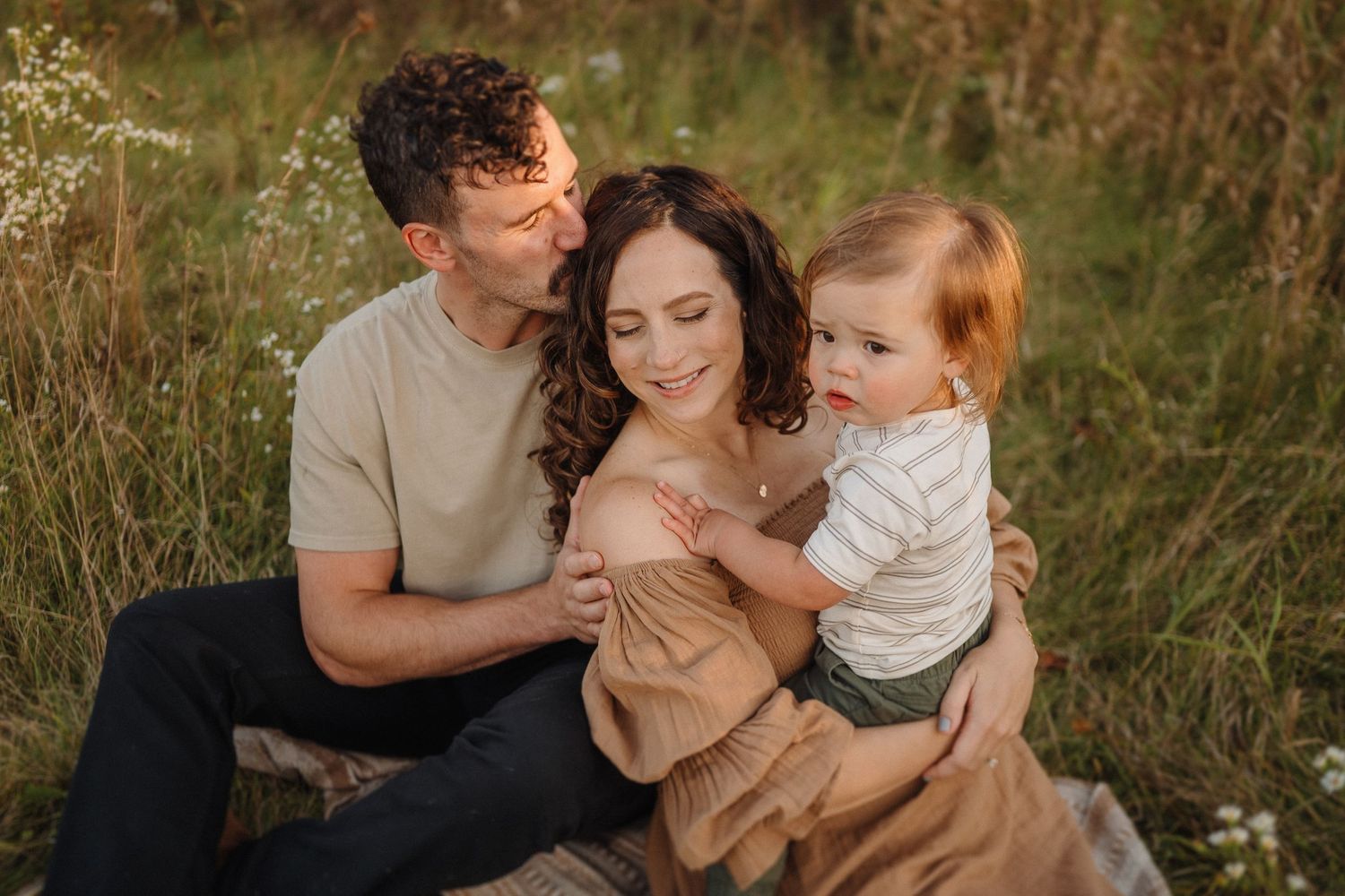 A family shares an intimate moment while sitting in tall grass during golden hour.