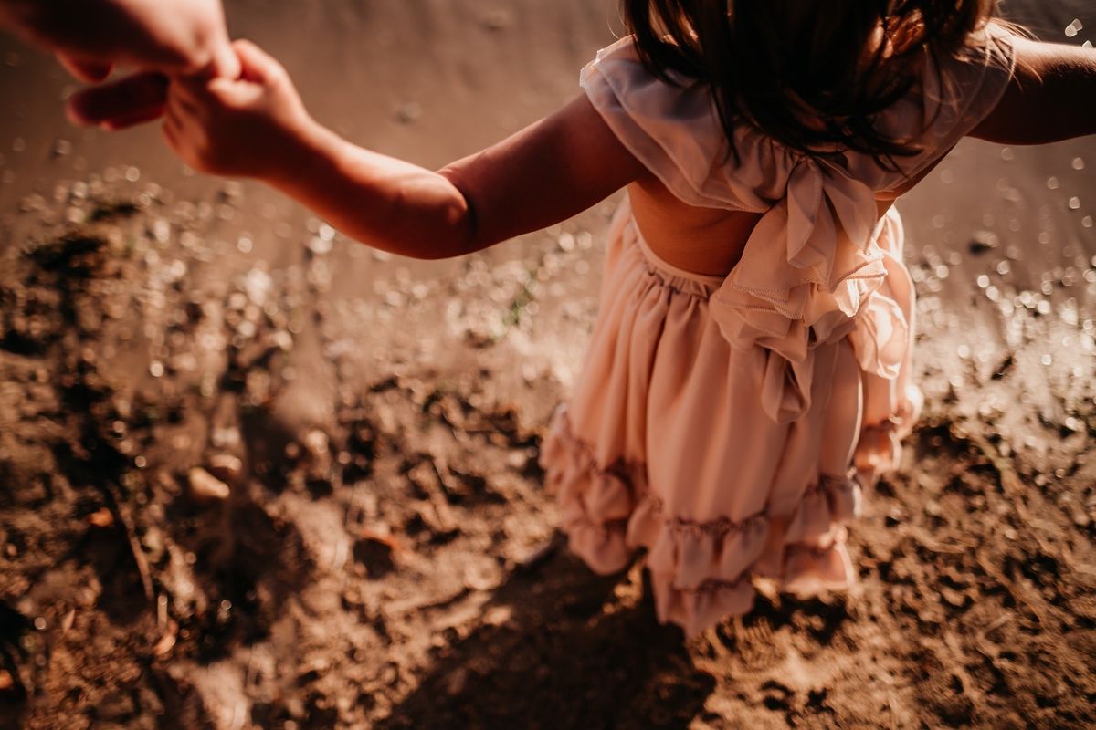 Close-up view of a pink ruffled dress against textured dirt ground in warm lighting.