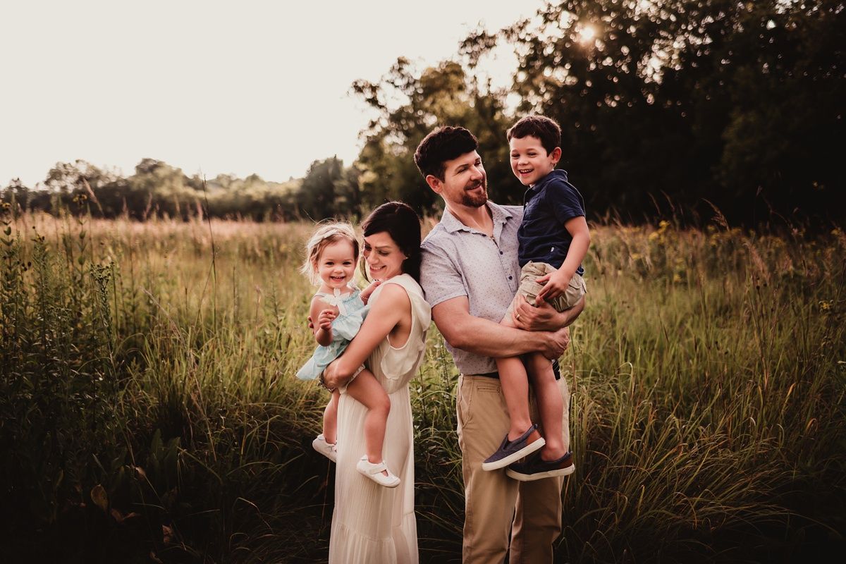 A family of four poses together in a golden sunlit field during sunset.