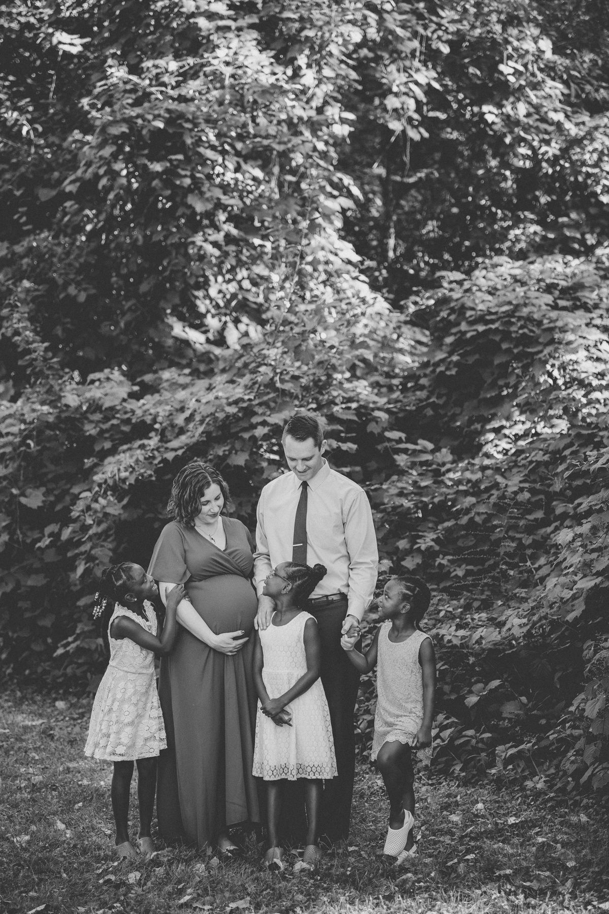 Black and white family portrait in wooded setting with natural lighting.