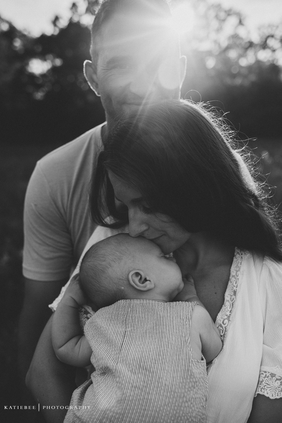Intimate black and white portrait of family with baby during sunset in outdoor setting.