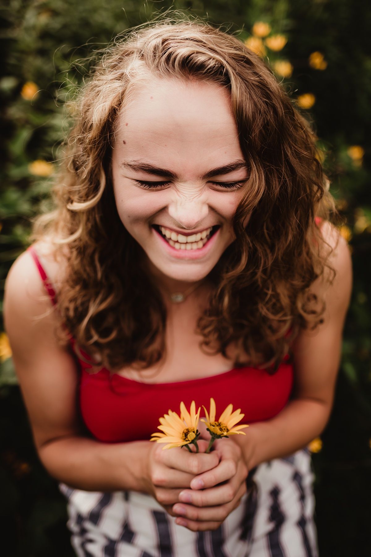 Joyful summer portrait with red top holding sunflowers against garden background.