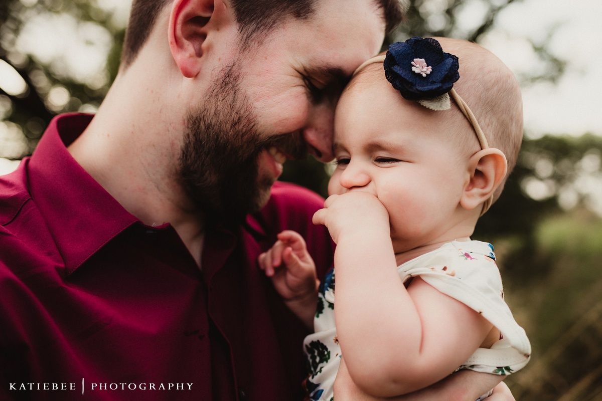 Baby wearing navy flower headband laughs while being held close.