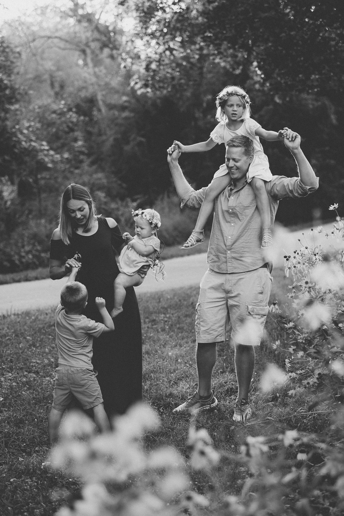 Black and white family portrait in natural setting surrounded by delicate white flowers.