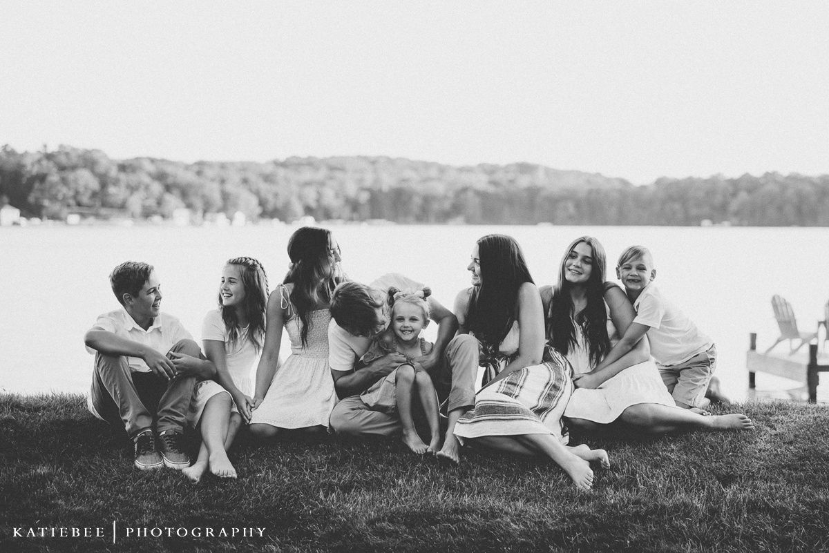 A group relaxes together on grass by a lake shore in black and white.