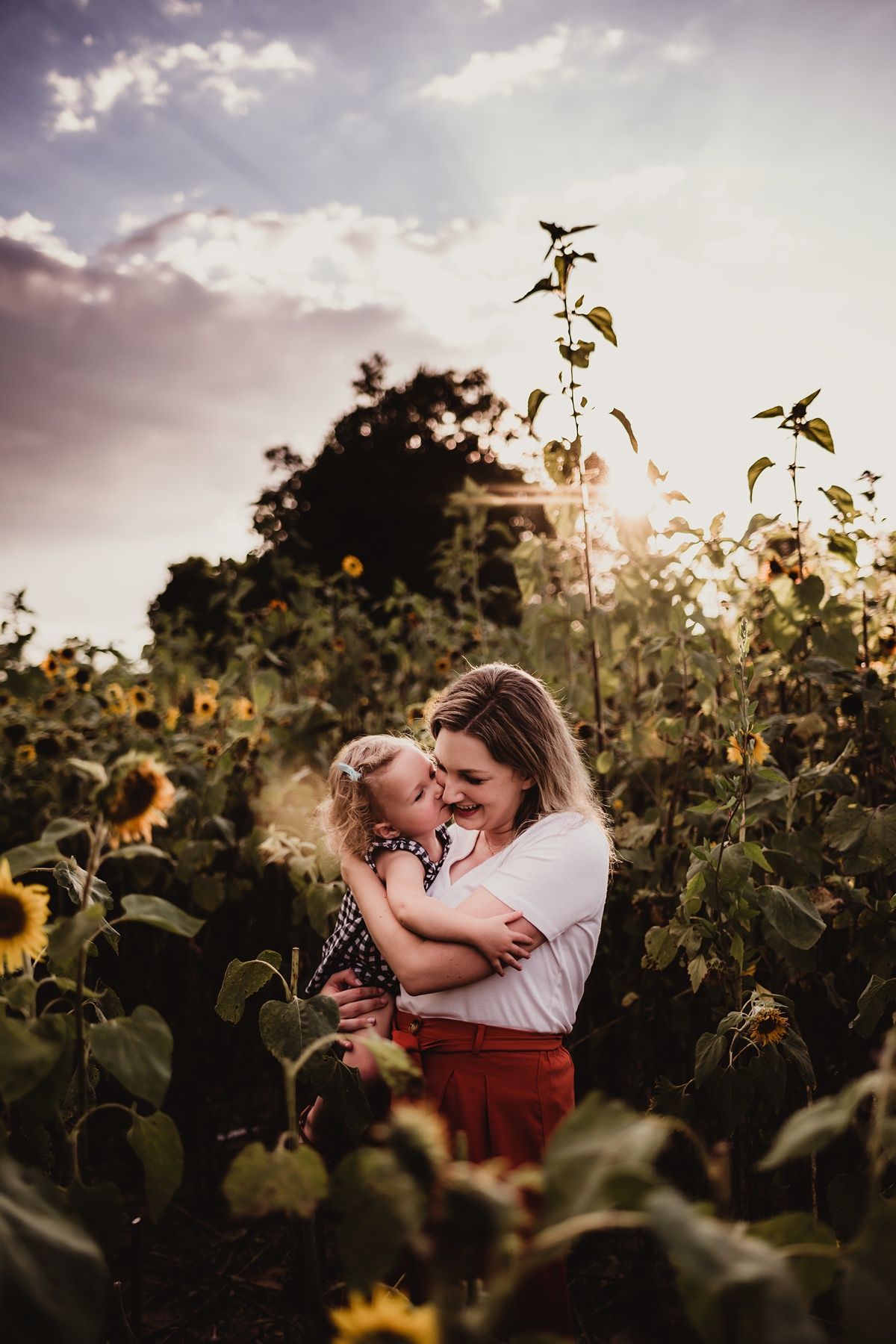 Intimate family moment captured in sunflower field at sunset.