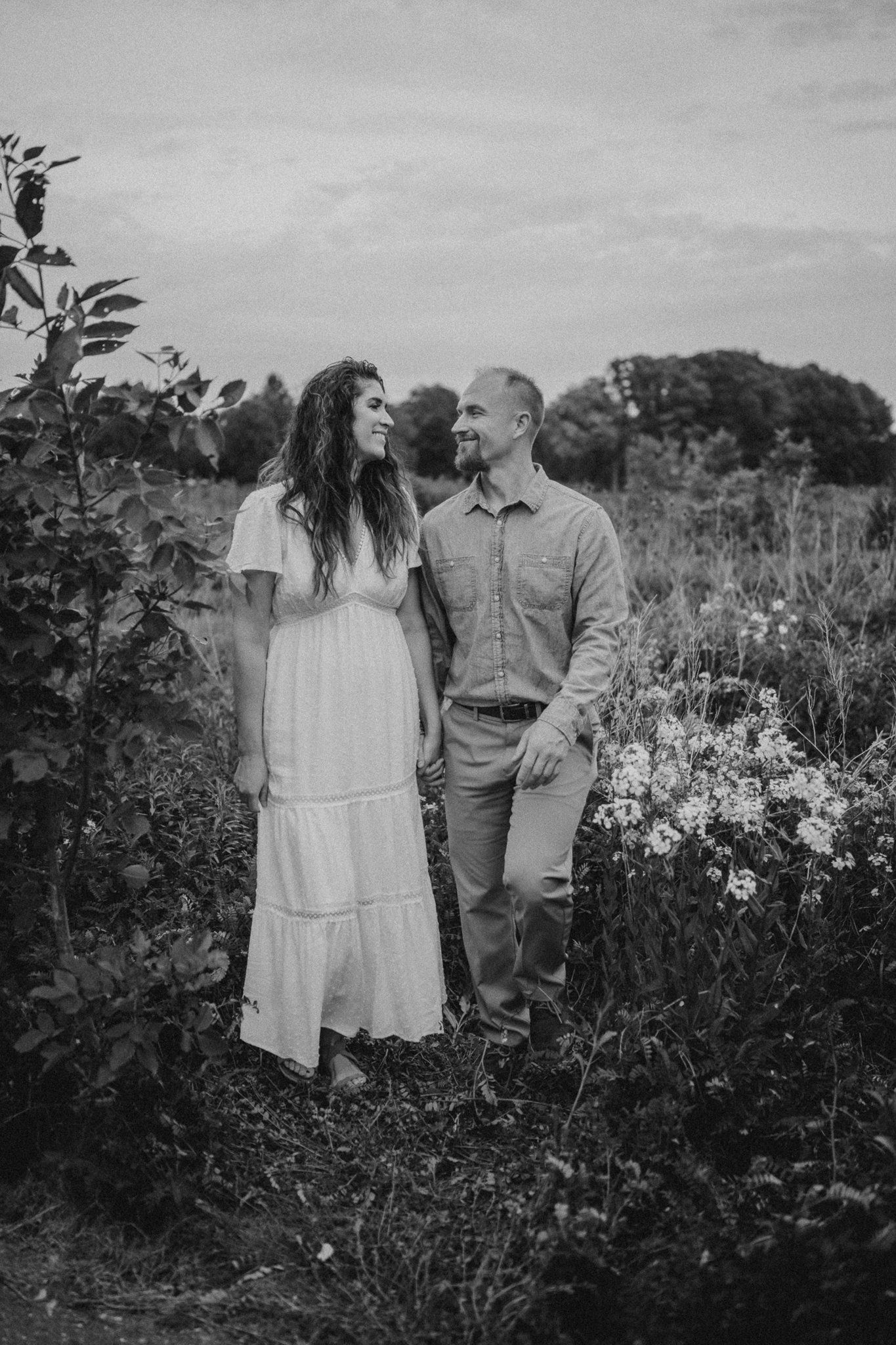 A black and white portrait of a couple standing together in a blooming garden at dusk.