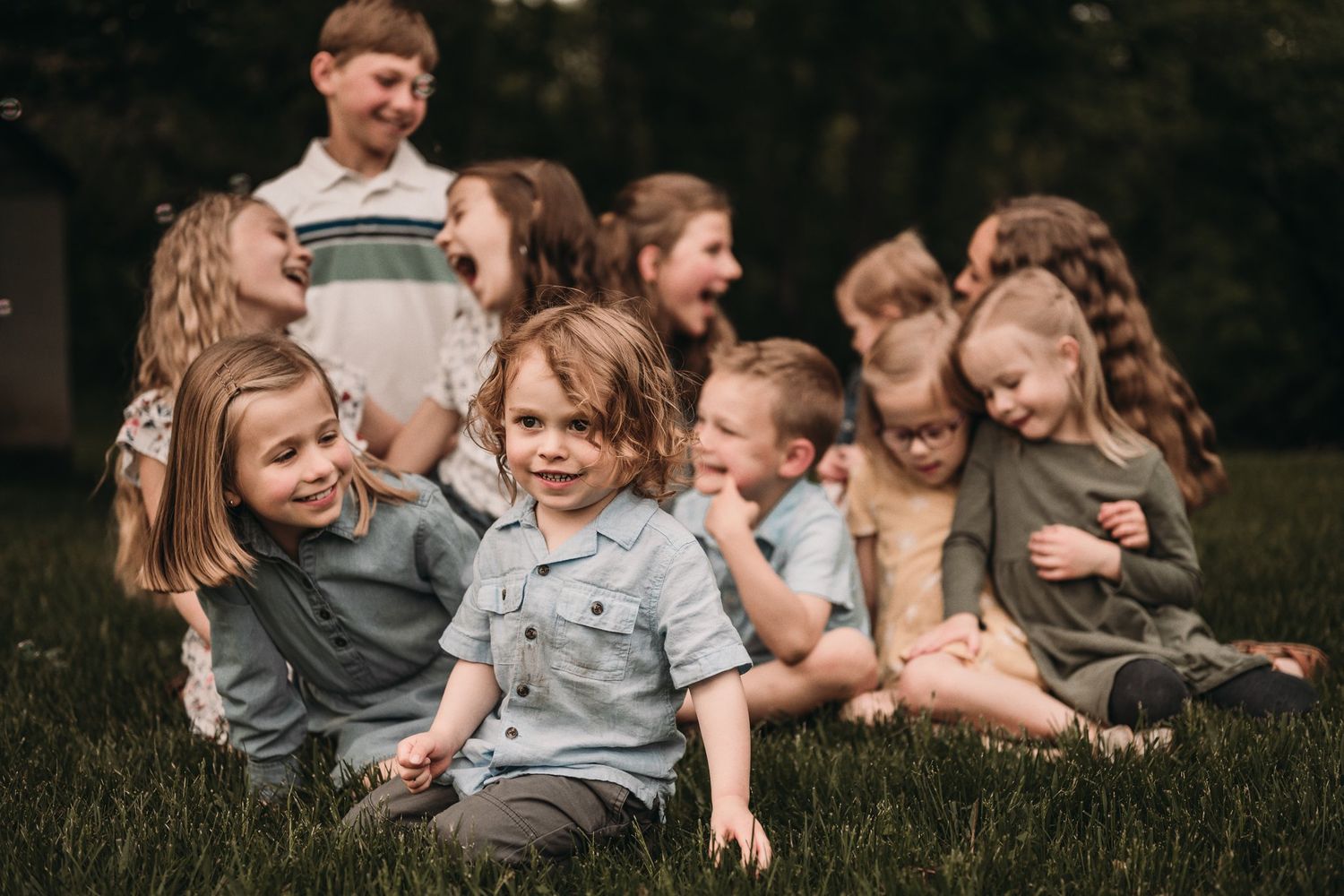 Group of children sitting together on grass during a casual outdoor photoshoot.