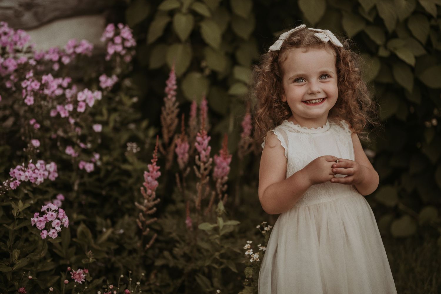 A sweet garden portrait features white lace against blooming pink flowers and green foliage.