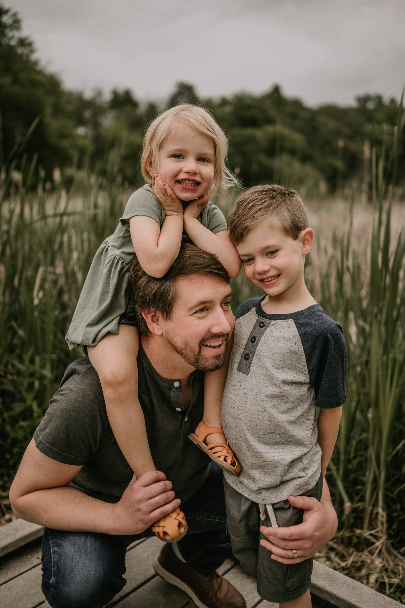 Happy family portrait on a wooden walkway with tall grass in the background.