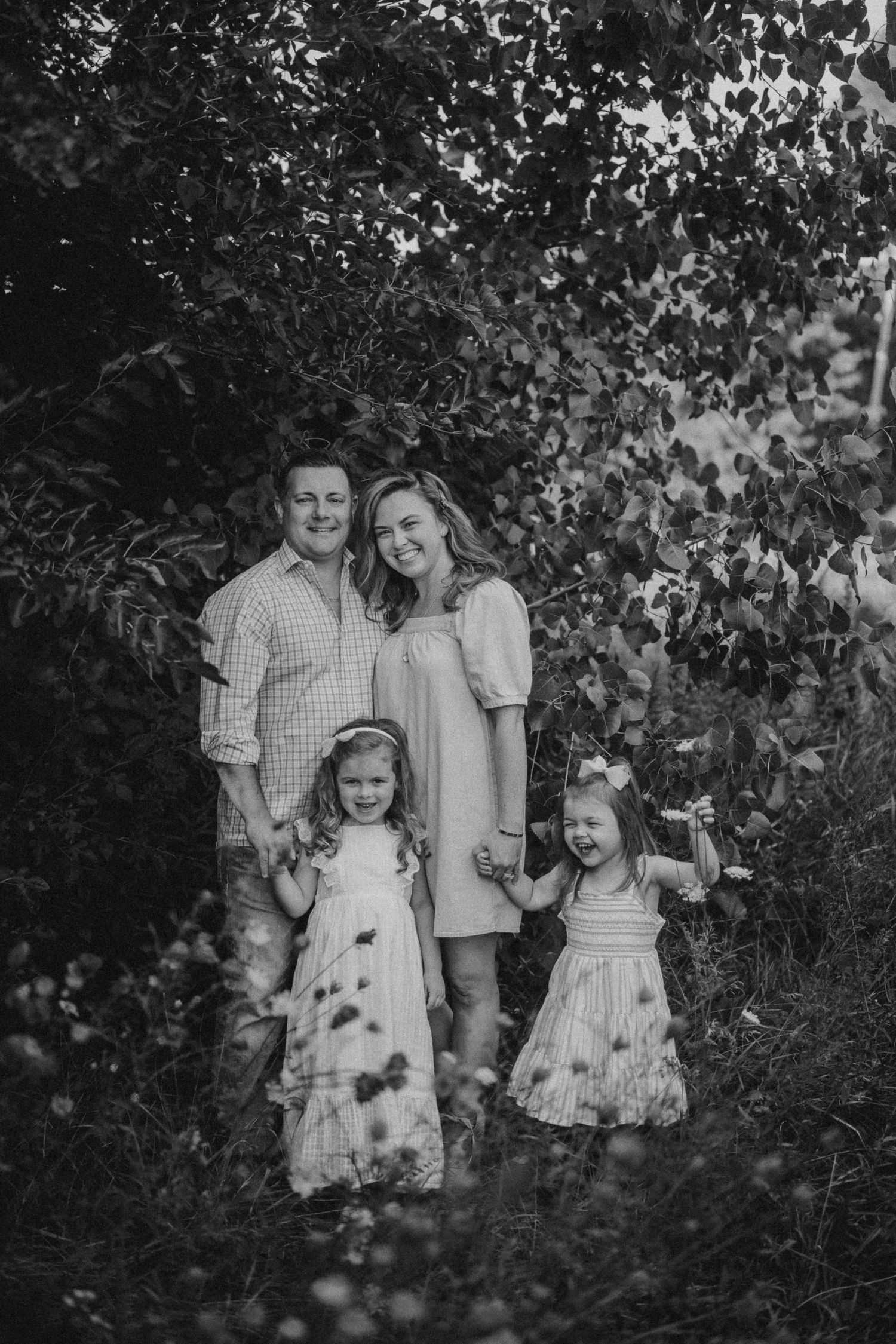 Black and white family portrait with children in matching dresses against leafy background.